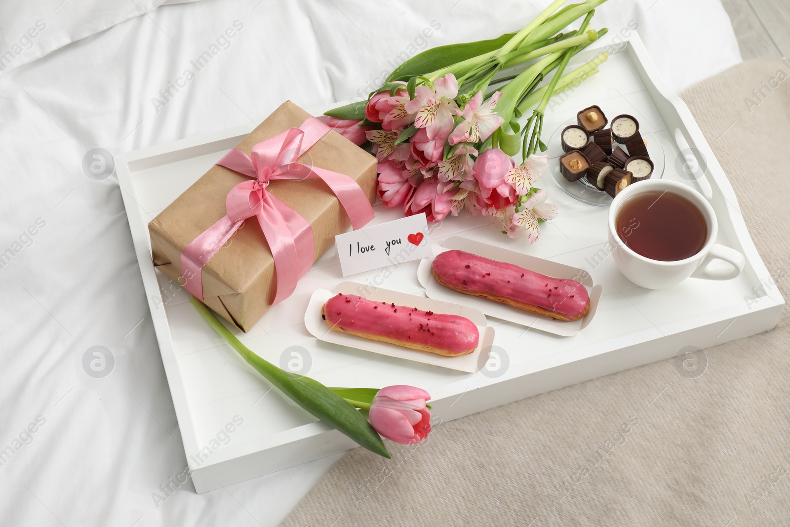 Photo of Tasty breakfast served in bed. Delicious desserts, tea, flowers, gift box and card with phrase I Love You on tray