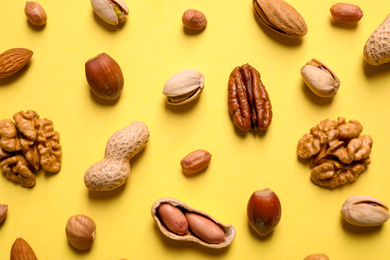 Different delicious nuts on yellow background, flat lay