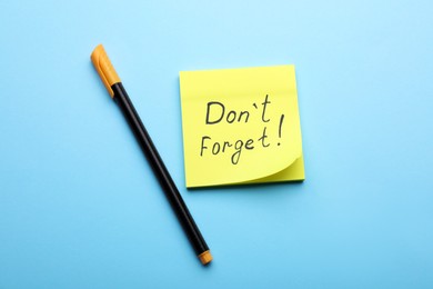 Photo of Paper note with phrase Don't Forget and pen on light blue background, flat lay