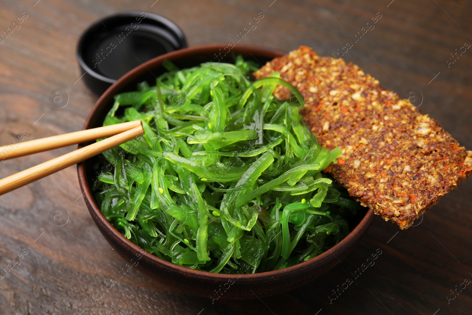 Photo of Tasty seaweed salad in bowl served on wooden table, closeup