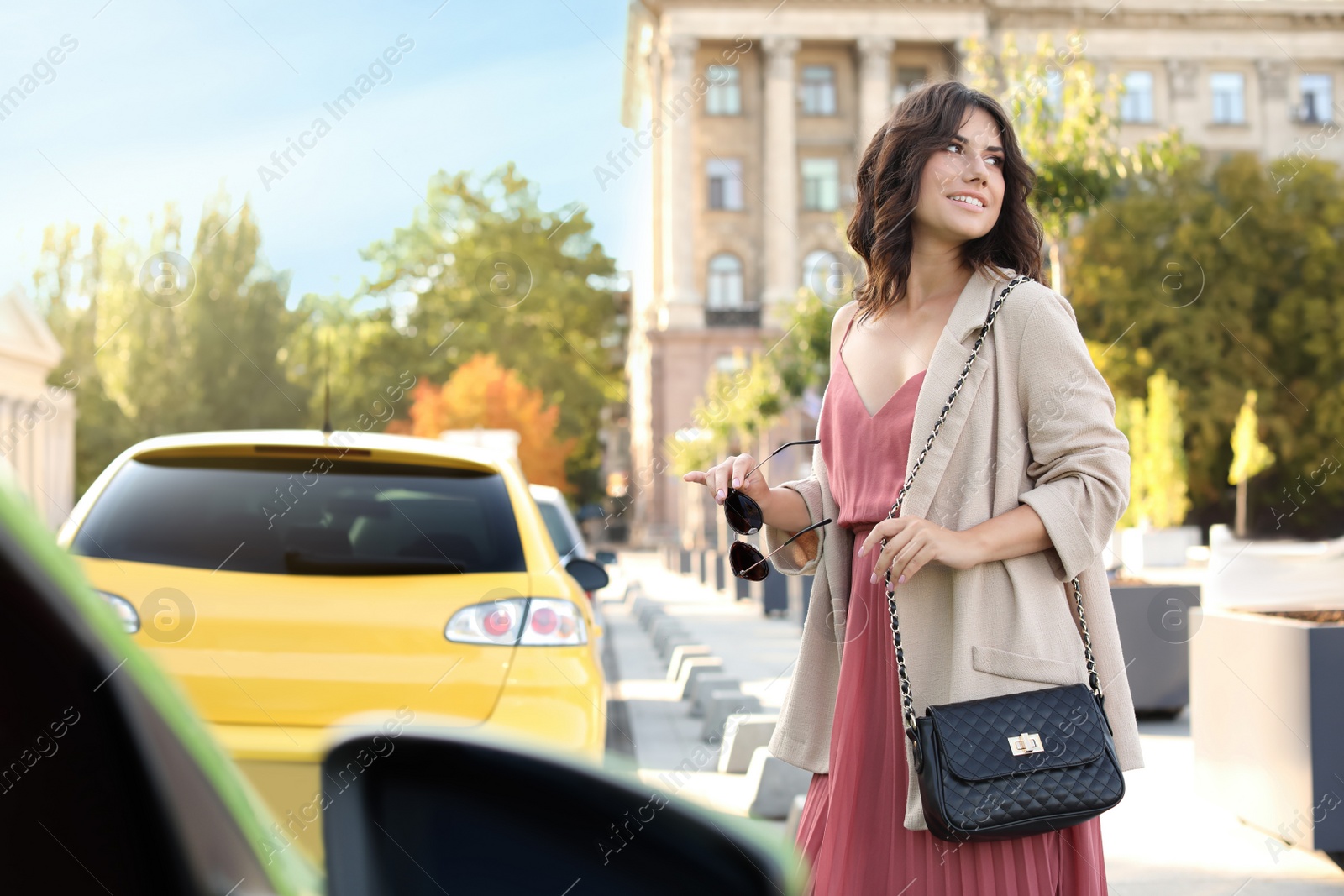 Photo of Young woman with stylish black bag and sunglasses on city street