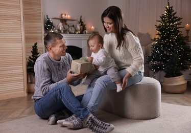 Happy couple with cute baby and gift in room decorated for Christmas