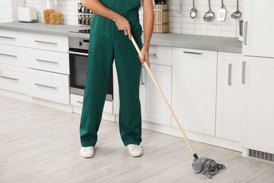 Male janitor cleaning floor with mop in kitchen