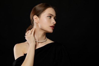 Photo of Young woman wearing elegant pearl jewelry on black background, space for text