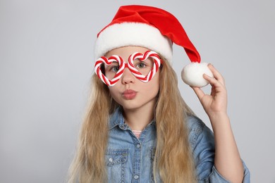 Photo of Girl wearing decorative Christmas eyeglasses in shape of hearts and Santa hat on light grey background