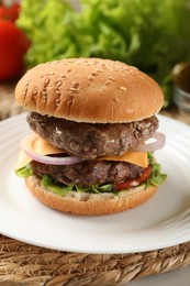 Photo of Tasty hamburger with patties, cheese and vegetables on wicker mat, closeup