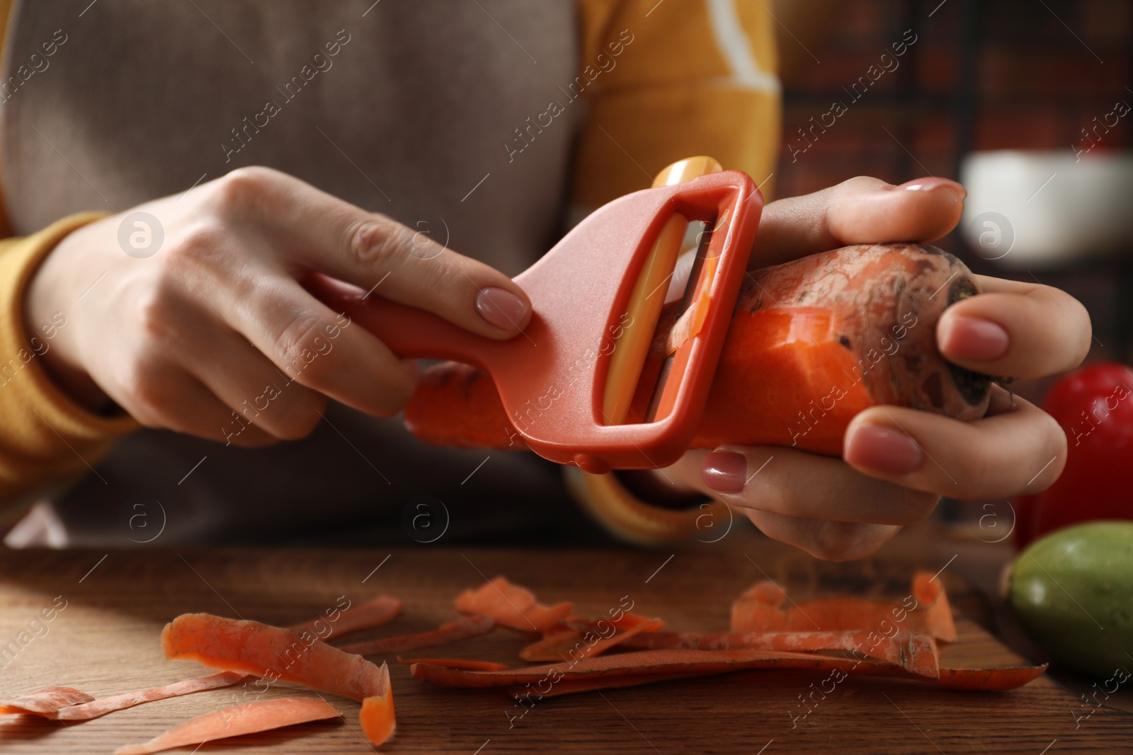 Photo of Woman peeling fresh carrot at wooden table indoors, closeup