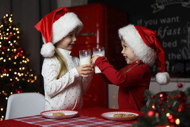 Photo of Cute little children with milk at table in dining room. Christmas time