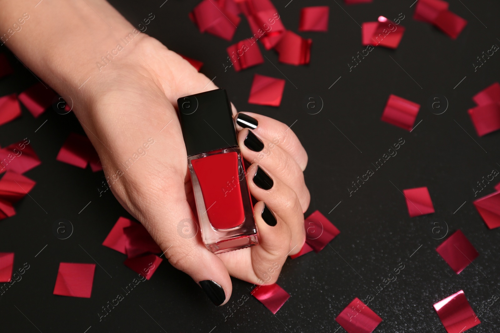 Photo of Woman with black manicure holding nail polish bottle on dark background, closeup. Space for text