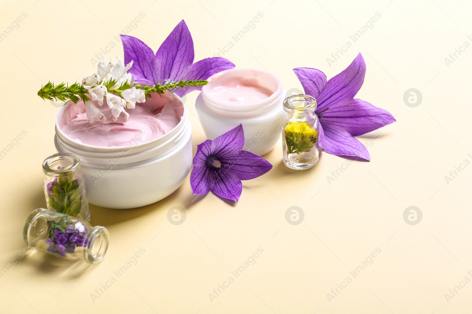 Photo of Composition with jars of body cream and flowers on beige background