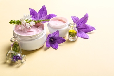 Composition with jars of body cream and flowers on beige background