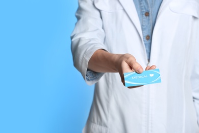 Doctor holding business card on color background, closeup with space for text. Dental medical service