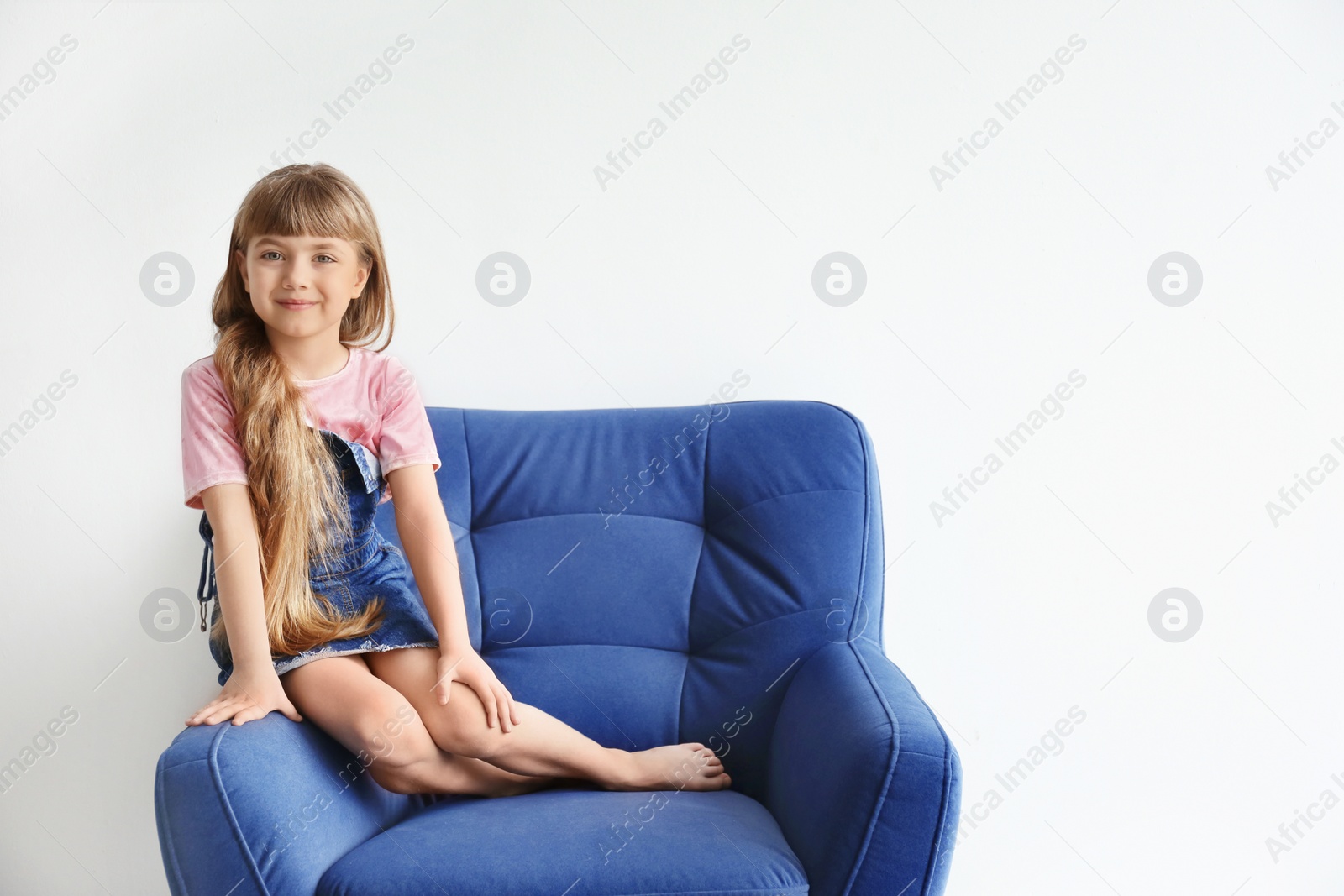 Photo of Portrait of cute little girl on armchair against white wall