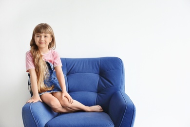 Photo of Portrait of cute little girl on armchair against white wall