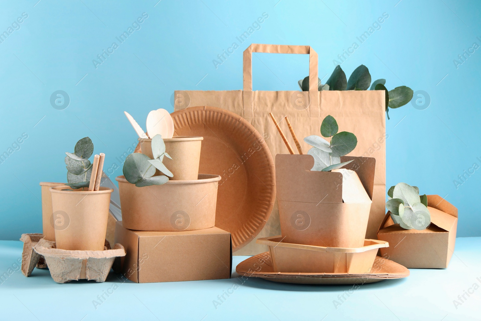 Photo of Eco friendly food packaging. Paper containers, tableware, bag and eucalyptus branches on white table against light blue background