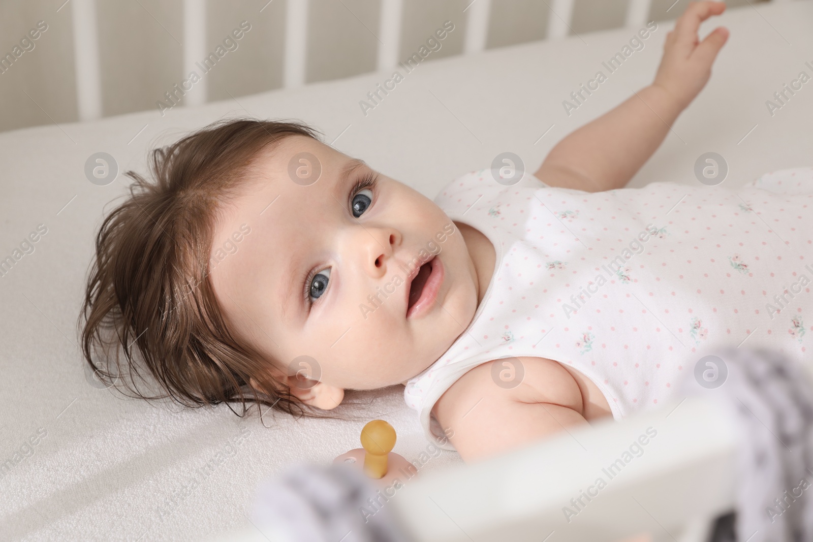 Photo of Cute little baby lying in comfortable crib at home