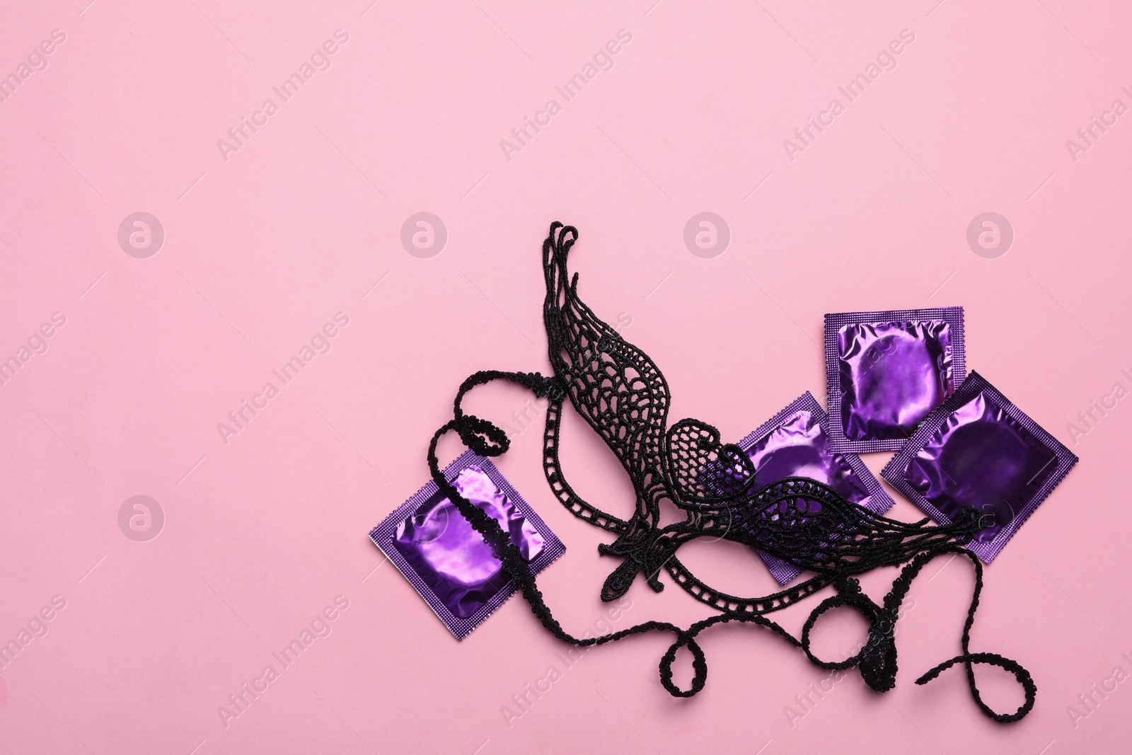 Photo of Lace mask and condoms on pink background, top view with space for text. Sex game