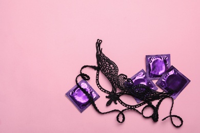 Photo of Lace mask and condoms on pink background, top view with space for text. Sex game