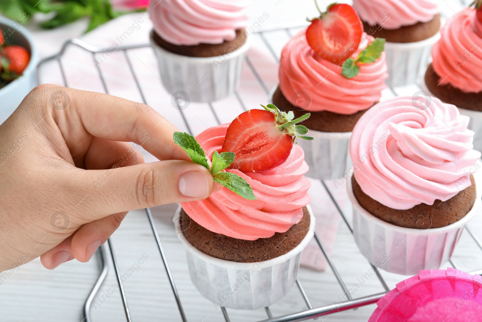 Photo of Woman decorating delicious cupcakes with mint at white wooden table, closeup