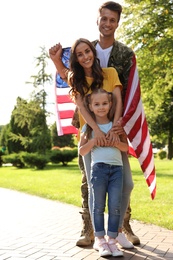 Photo of Man in military uniform with American flag and his family at sunny park