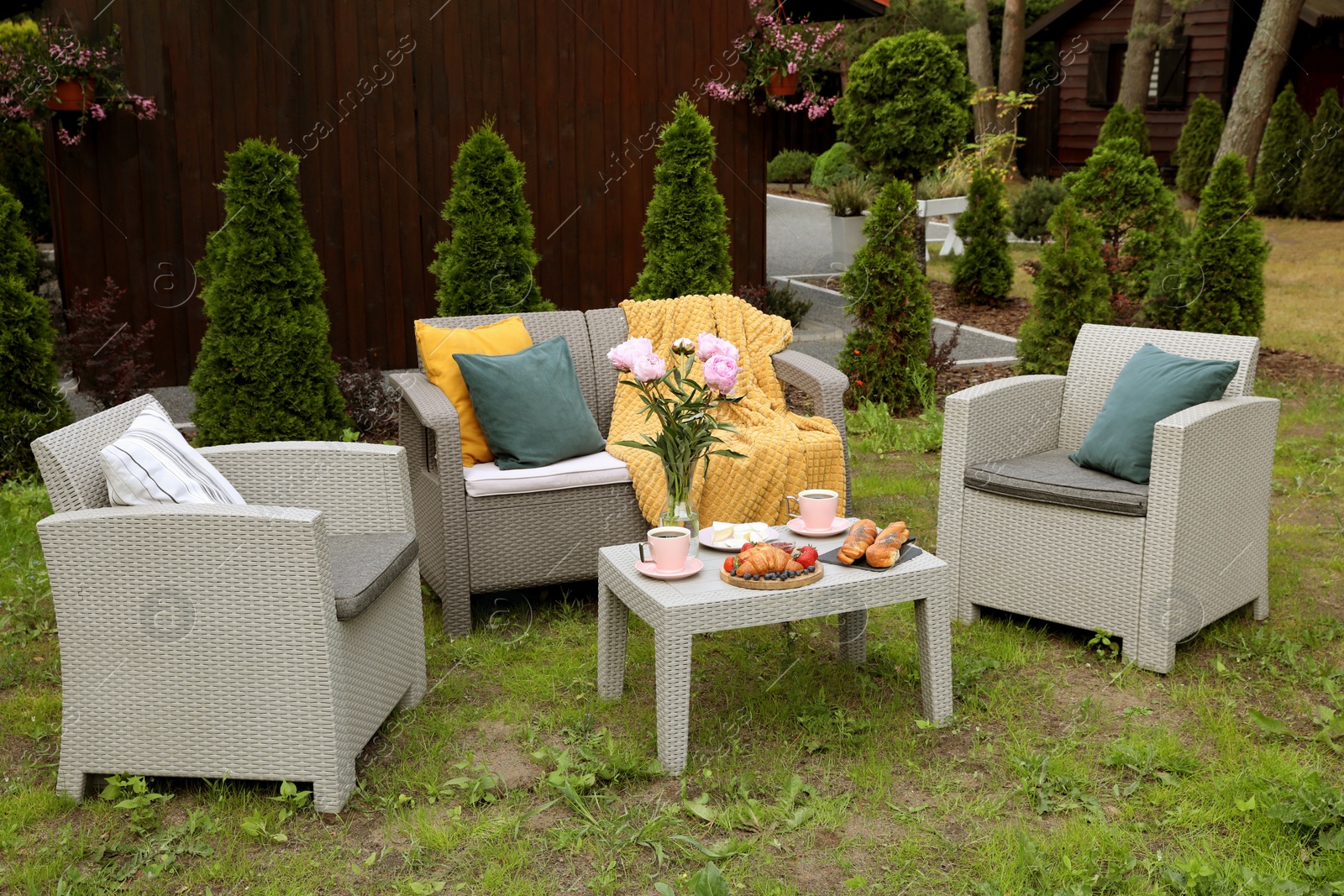 Photo of Breakfast served outdoors. Morning drink, food and vase with flowers on rattan table