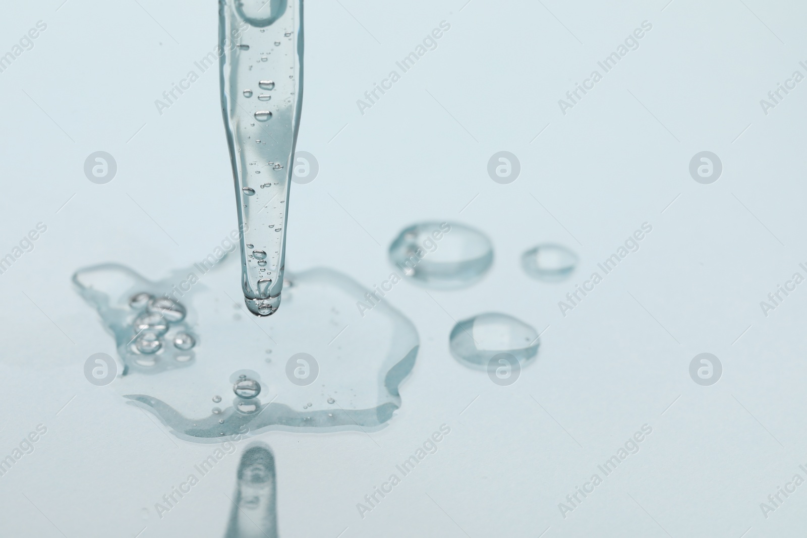 Photo of Glass pipette and transparent liquid on light background, closeup. Space for text