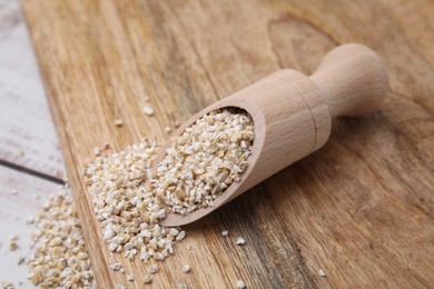 Photo of Scoop with raw barley groats on light wooden table, closeup