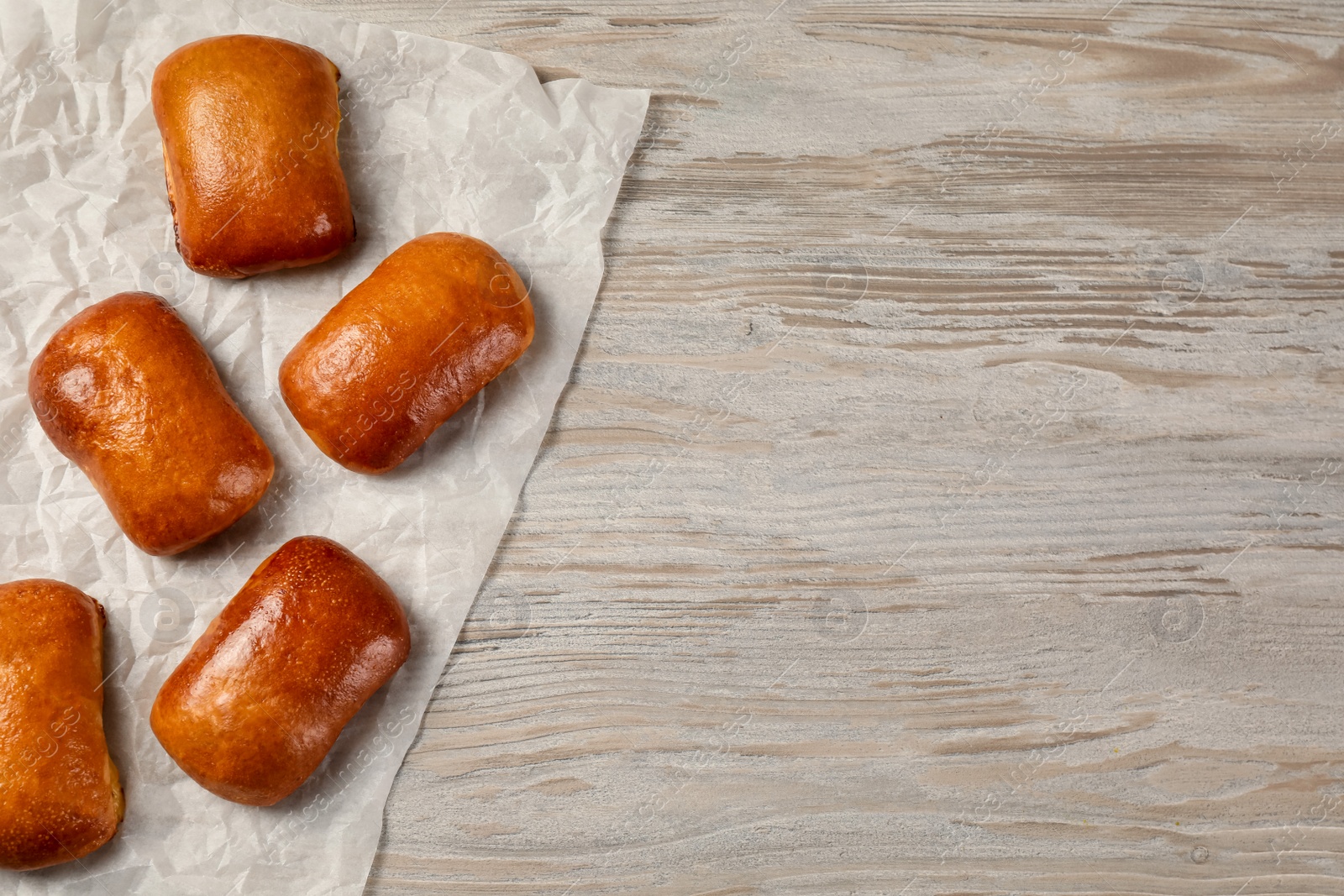 Photo of Delicious baked pirozhki on wooden table, flat lay. Space for text