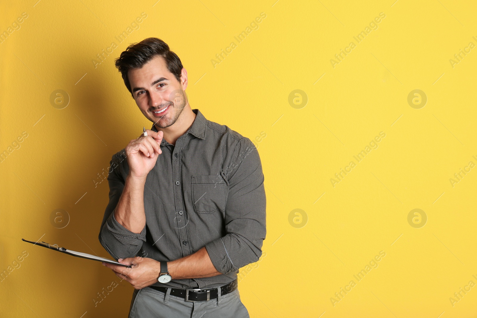 Photo of Young male teacher with clipboard on yellow background. Space for text