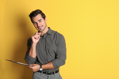 Young male teacher with clipboard on yellow background. Space for text