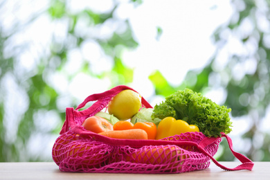Photo of Net bag with vegetables on table against blurred background