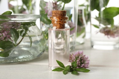 Photo of Beautiful clover flower and bottle of essential oil on white wooden table