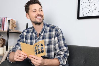 Photo of Happy man holding greeting card on sofa in living room