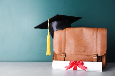 Photo of Graduation hat with briefcase and diploma on table near chalkboard. Space for text