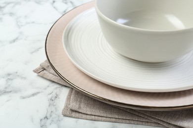 Photo of Clean plates, bowl and napkin on white marble table, closeup. Space for text