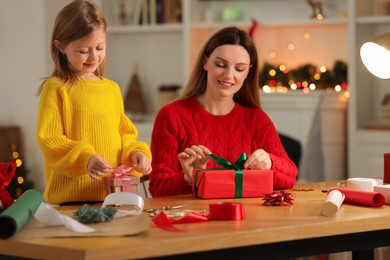 Christmas presents wrapping. Mother and her little daughter decorating gift boxes with ribbon at home