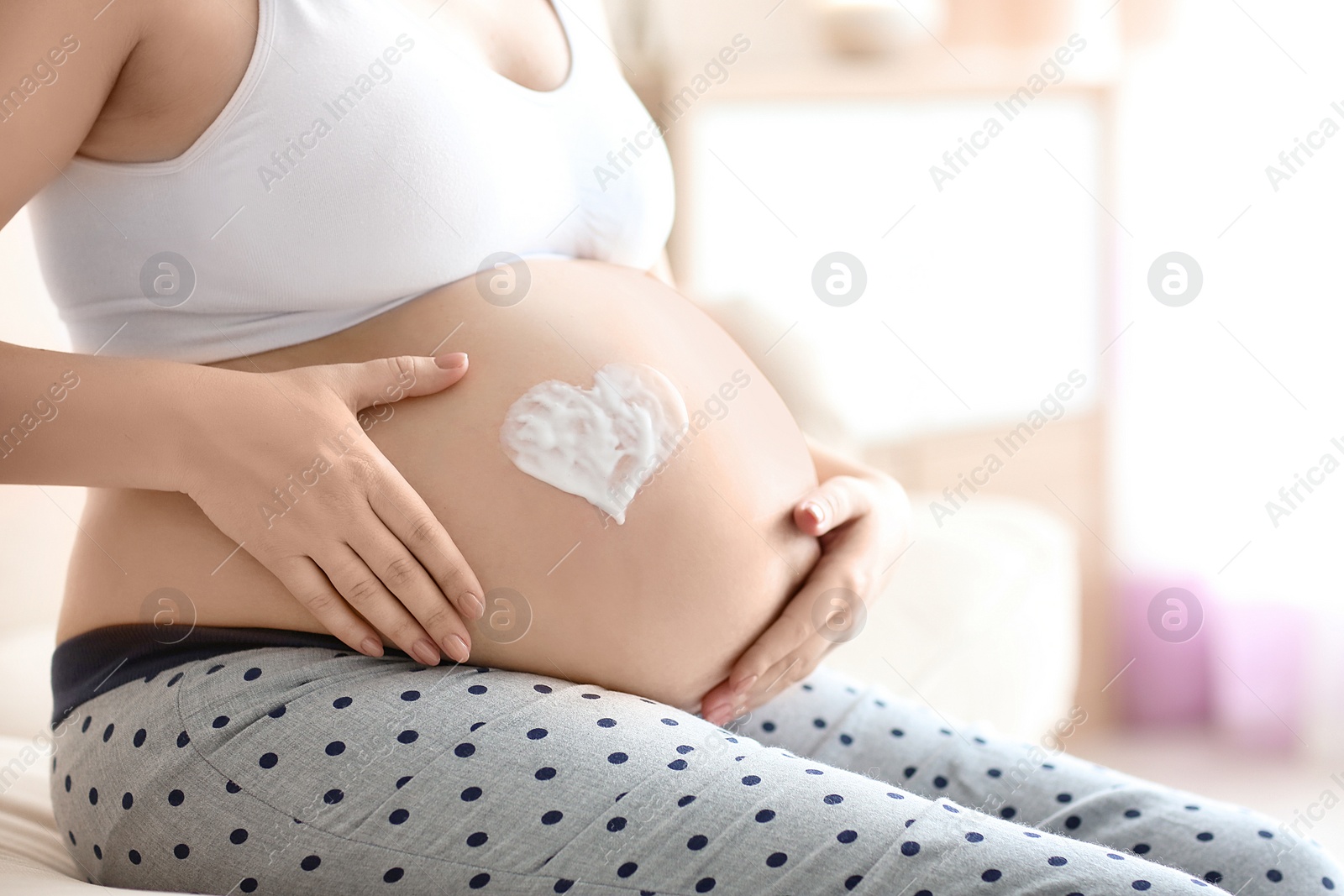 Photo of Heart painted with cream on pregnant woman's belly against blurred background, closeup