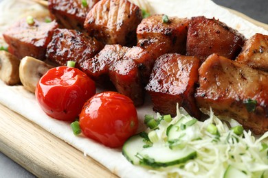 Photo of Delicious shish kebabs with vegetables and lavash on wooden board, closeup