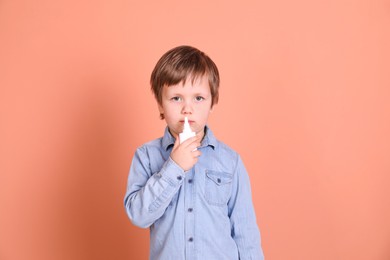 Photo of Sick little boy using nasal spray on coral background