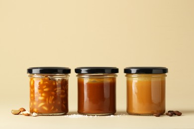 Photo of Tasty salted caramel in jars with peanuts, coffee beans and salt on pale yellow background