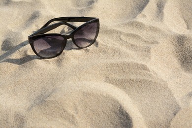 Stylish sunglasses with black frame on sandy beach, space for text