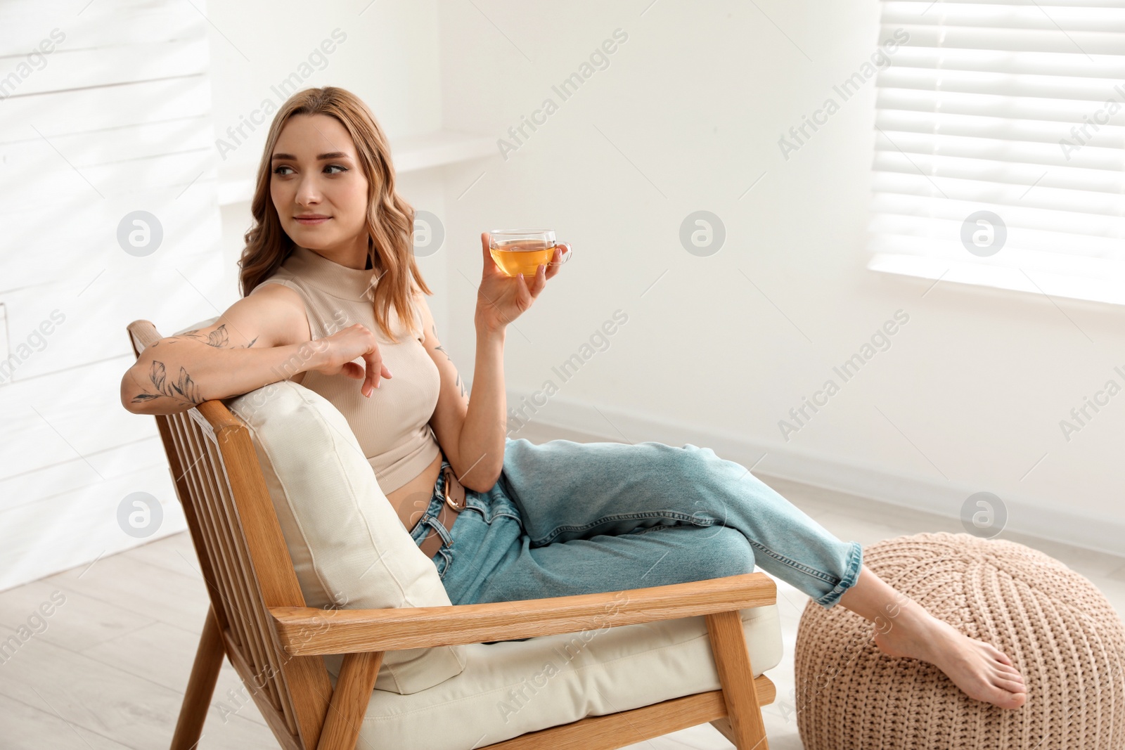 Photo of Beautiful woman with tattoos on arms drinking tea at home