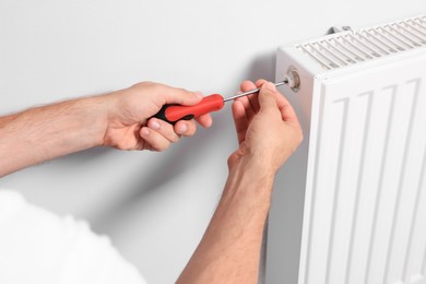 Photo of Professional plumber using screwdriver while preparing heating radiator for winter season, closeup