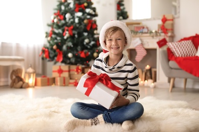 Cute little child in Santa hat with Christmas gift box at home