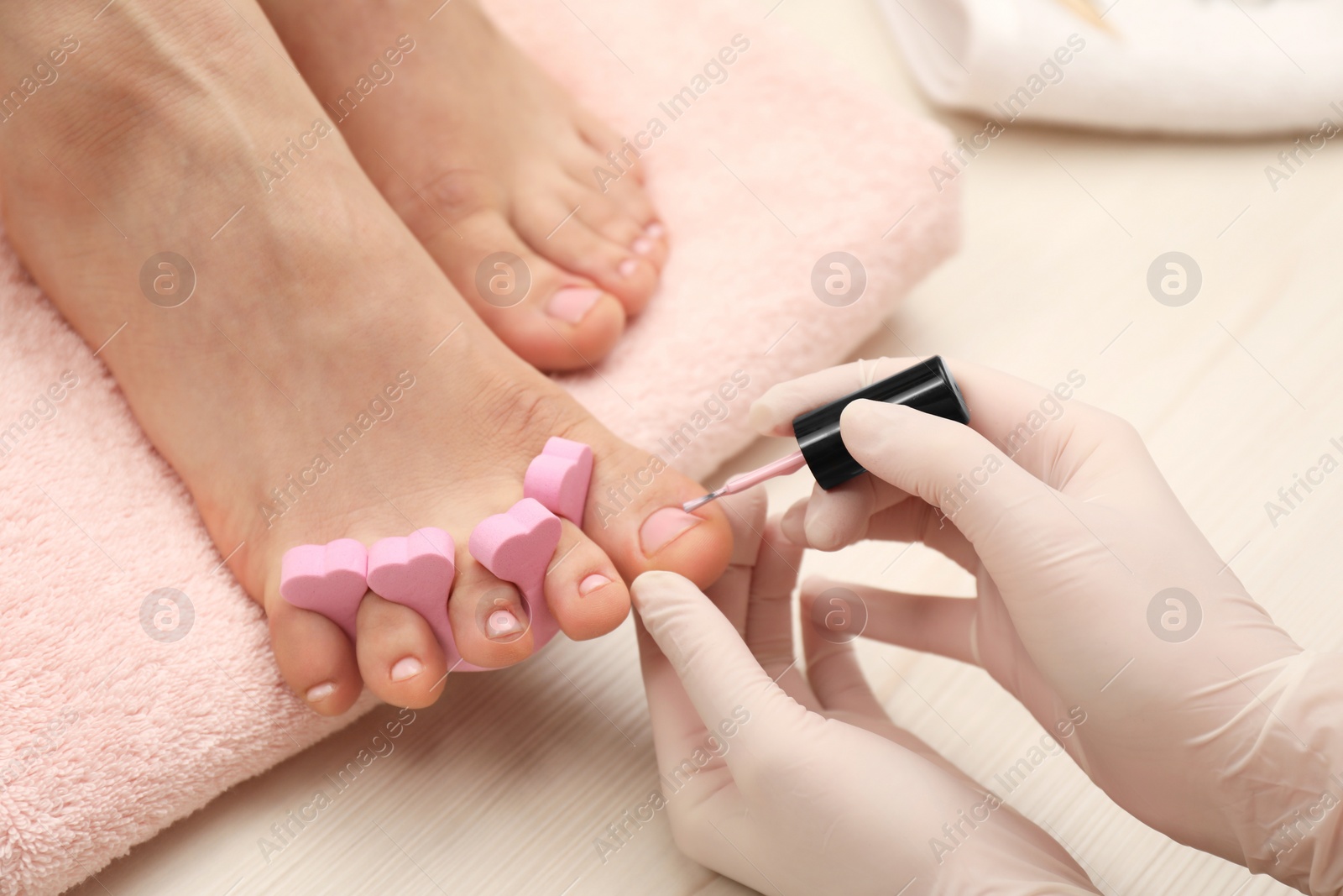 Photo of Professional pedicurist painting client`s toenails with polish in beauty salon, closeup