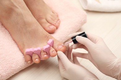 Professional pedicurist painting client`s toenails with polish in beauty salon, closeup