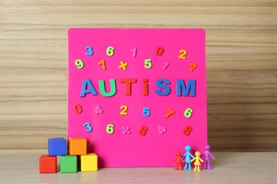 MYKOLAIV, UKRAINE - DECEMBER 30, 2021: Magnetic board with word Autism, colorful cubes and human figures on wooden table