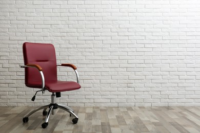 Comfortable office chair near white brick wall indoors. Space for text