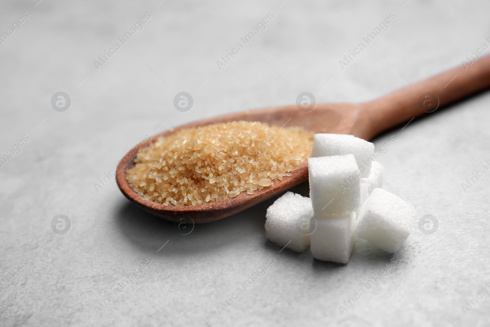 Photo of Refined cubes and brown sugar in spoon on grey background