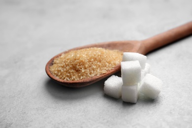 Photo of Refined cubes and brown sugar in spoon on grey background